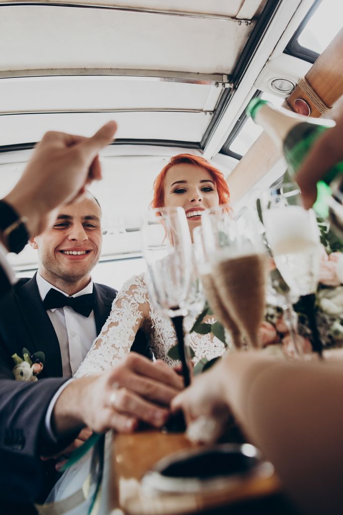 Stylish happy bride and groom toasting with glasses of champagne and having fun with bridesmaids and groomsmen inside of retro car. emotional moment, space for text. wedding party